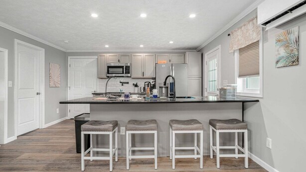 A modern kitchen with a central island, white cabinetry, and bar stools. - Grandpa's Cottage | Cute, clean and cozy studio apartment! (Chincoteague Island)