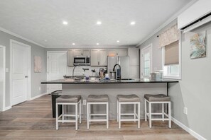 Een moderne keuken met een centraal kookeiland, witte kastjes en barstoelen.