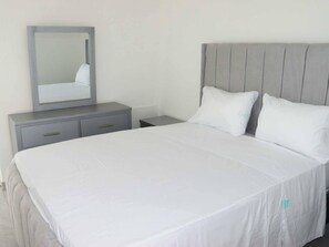 A neatly arranged bedroom with a large bed, a bedside table, a nightstand, and a mirror. - Condo Neuf a Sosua Près de Tout 304 (Sosúa)