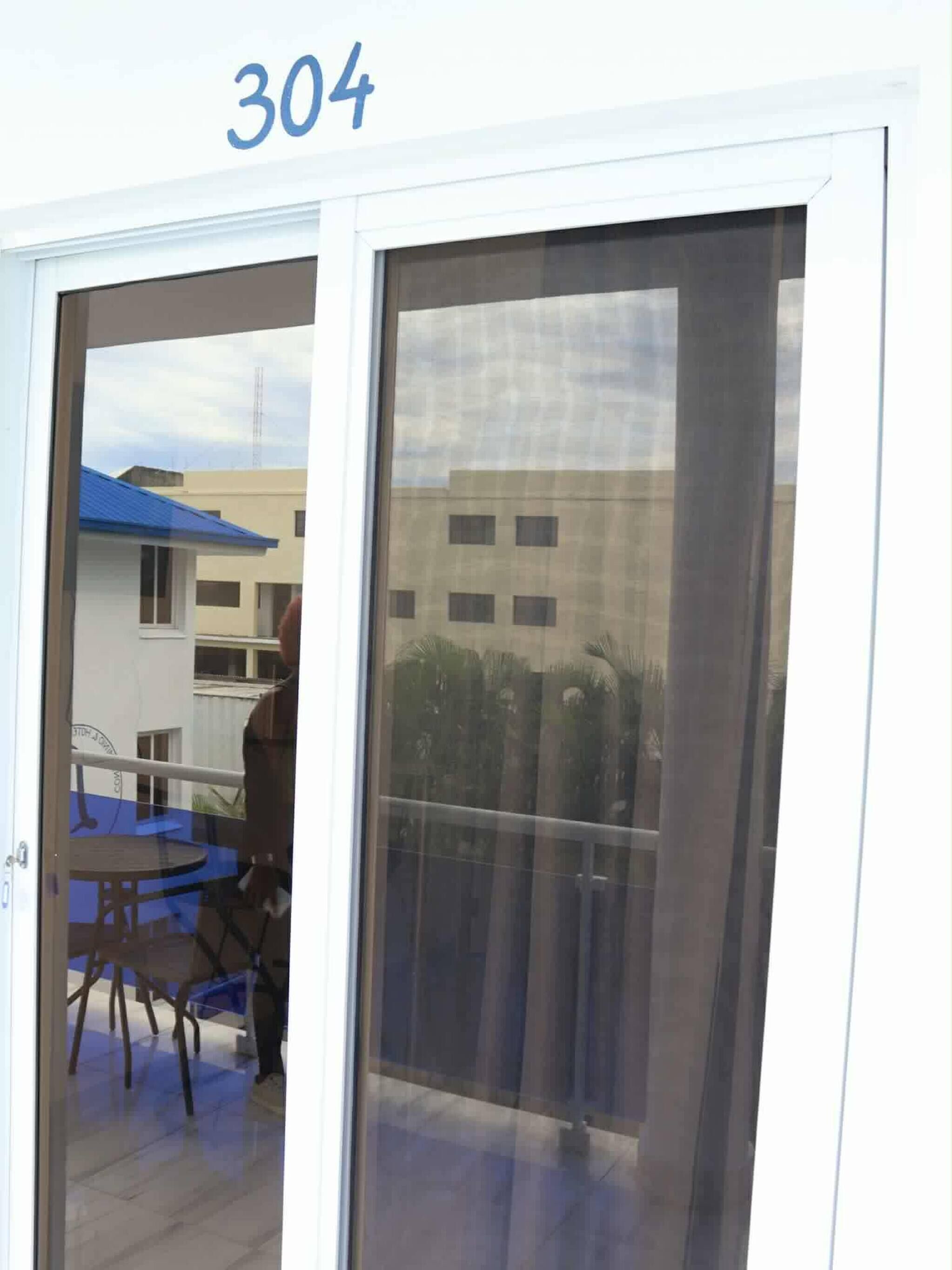 Quarto com porta de correr de vidro, varanda com vista para edifícios e mesa com cadeiras.