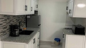 A kitchen with white cabinets, a granite countertop, a coffee maker, and a microwave. - Condo Neuf Sosua 3 Minutes de la Plage 208 (Sosúa)