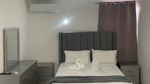A bedroom with a bed, bedside tables, a mirror, a ceiling light fixture, and a window with curtains. - Condo Neuf Sosua 3 Minutes de la Plage 208 (Sosúa)