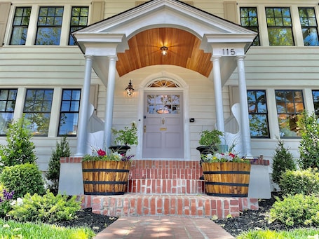 A two-story house with a front porch, a wooden door, and a number '115' above the door.