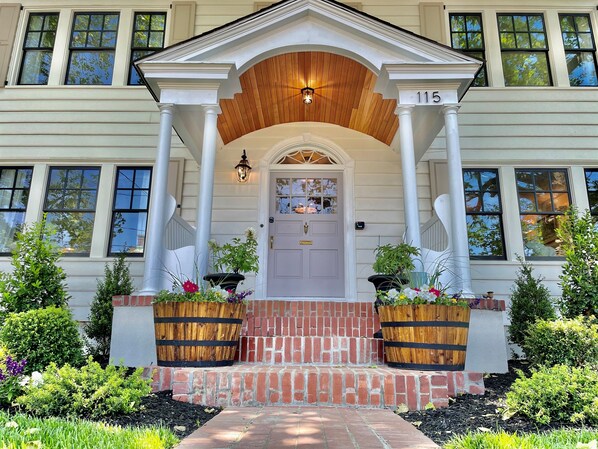 A two-story house with a front porch, a wooden door, and a number '115' above the door.