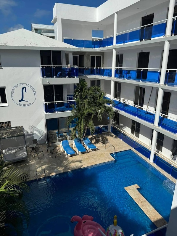 A multi-story hotel with a pool area, including lounge chairs and a palm tree. - Condo Neuf, Balcon en Plein Coeur de Sosua, 205 (Sosúa)
