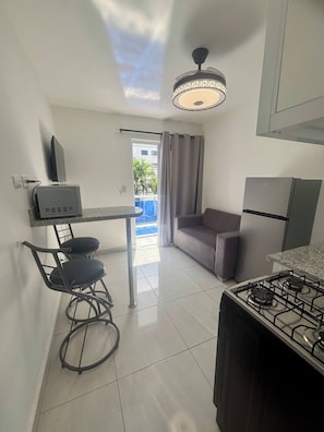 A compact kitchen with a gas stove, a small dining table with chairs, a sofa, and a ceiling light fixture. - Condo Neuf, Balcon en Plein Coeur de Sosua, 205 (Sosúa)