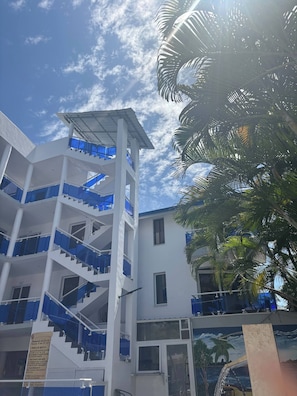 A multi-story building with a central staircase, balconies, and a clear sky. - Condo Neuf, Balcon en Plein Coeur de Sosua, 205 (Sosúa)