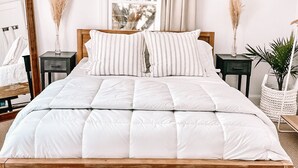 Een netjes ingerichte slaapkamer met een groot bed, een hanglamp, een raam met gordijnen en een kunstwerk aan de muur.