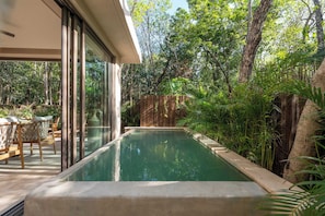 A swimming pool with a wooden deck and chairs, surrounded by lush greenery and trees. - Artila Haven | Amazing Jacuzzi with Open Views (Tulum)