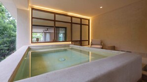 Un área de spa con un jacuzzi rectangular, una ventana con marco de madera y vistas a un jardín.