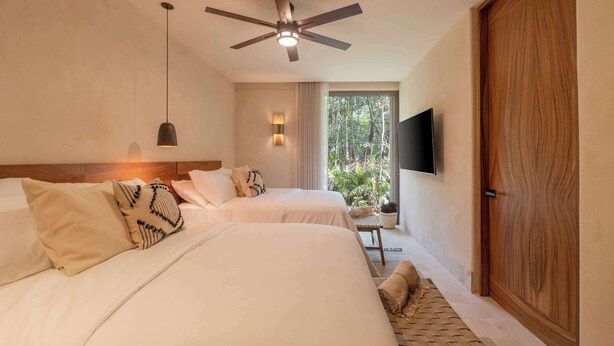 Une chambre d’hôtel avec deux lits, un ventilateur de plafond, un téléviseur fixé au mur et une vue sur la verdure environnante.