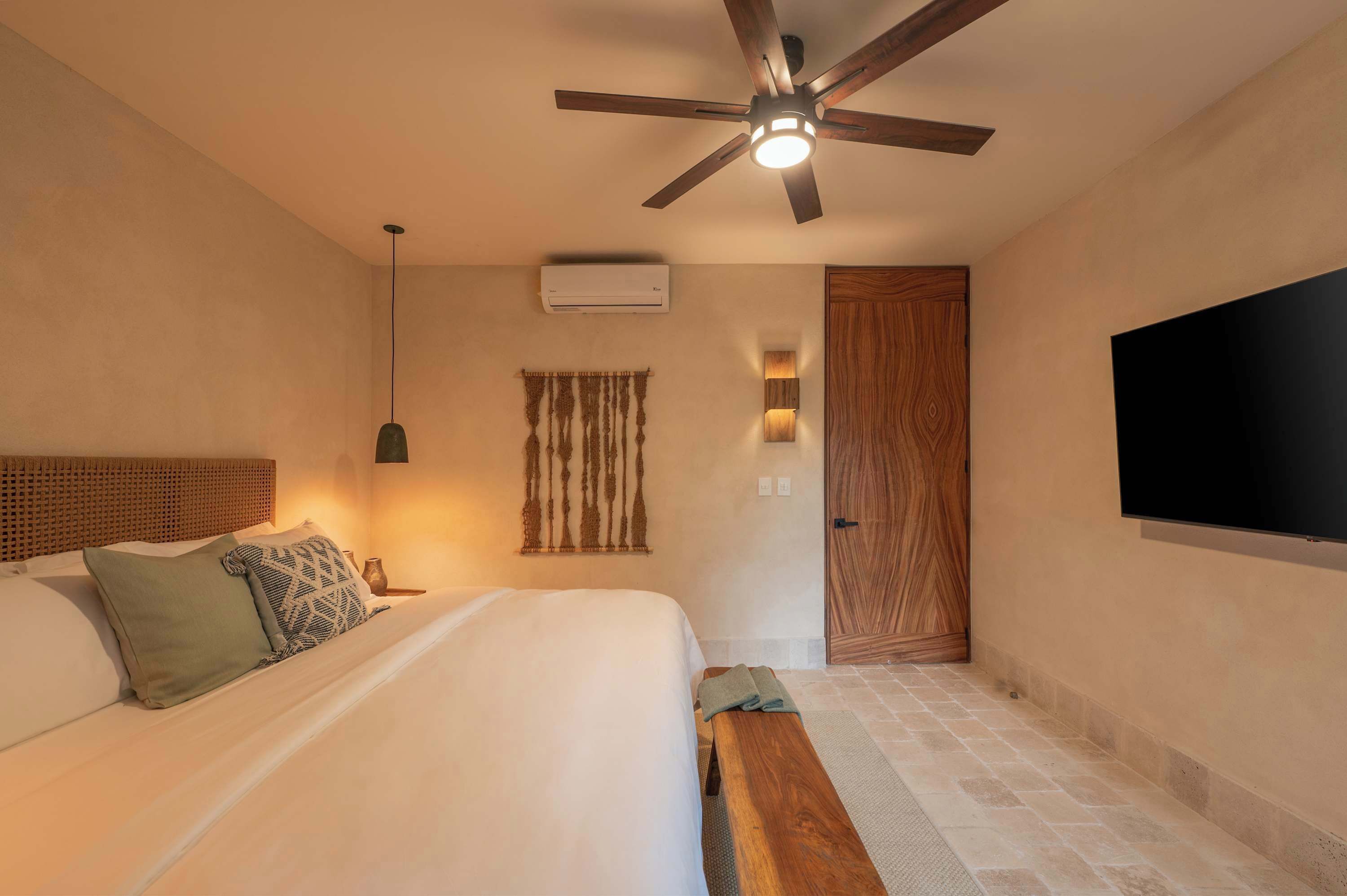 Ein Schlafzimmer mit Bett, Deckenventilator, Klimaanlage, Holztür und flachbildschirmfernseher an der Wand.