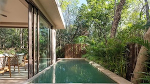 Una piscina con muelle de madera y sillas, rodeada de abundante vegetación y árboles.