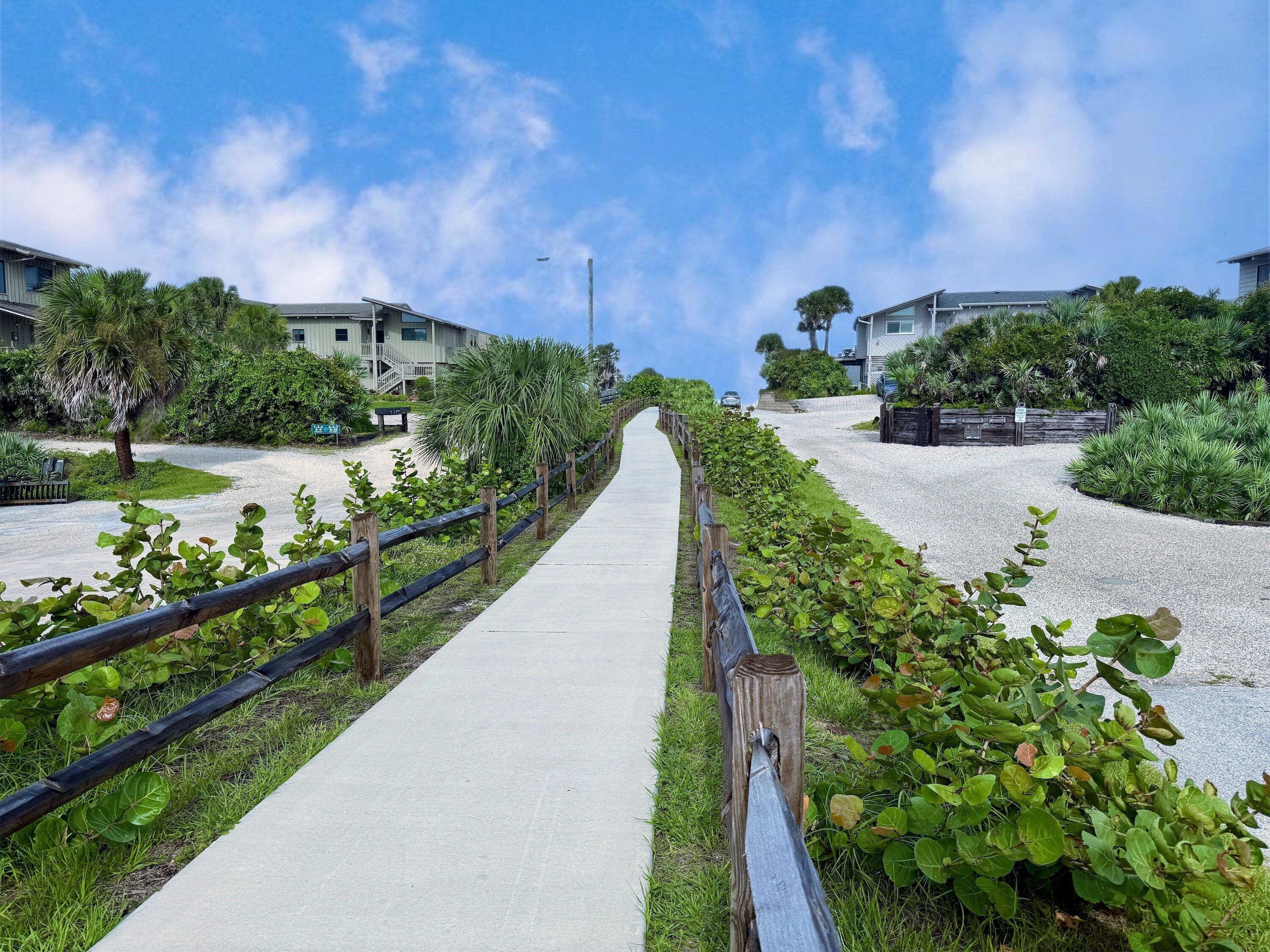 A pathway leading to a residential area with houses, a fence, and greenery.