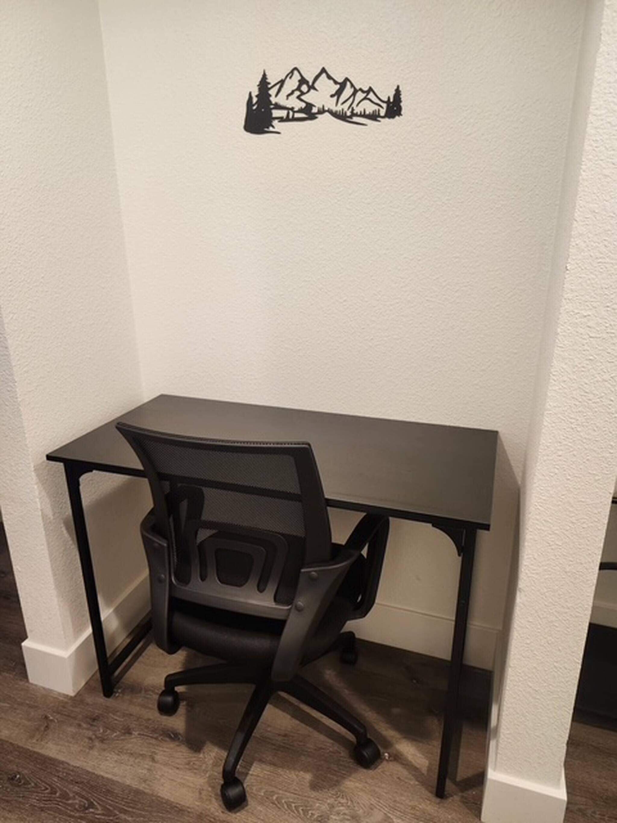 Ett hörnkontor med ett svart skrivbord och en svart stol, vita väggar och en väggdekor som föreställer ett berglandskap.