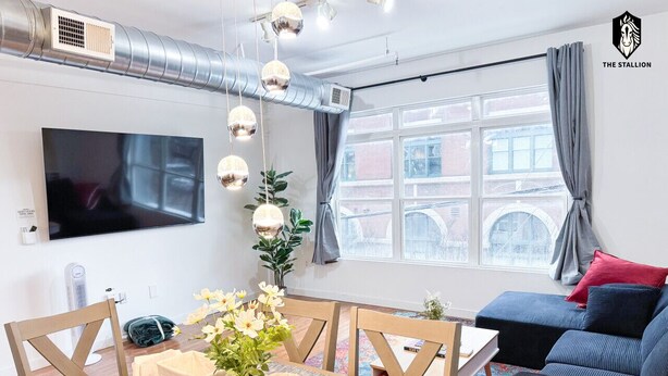 En moderne stue med stort fjernsyn, spisebord med stole, sofa og et vindue med gardiner.
