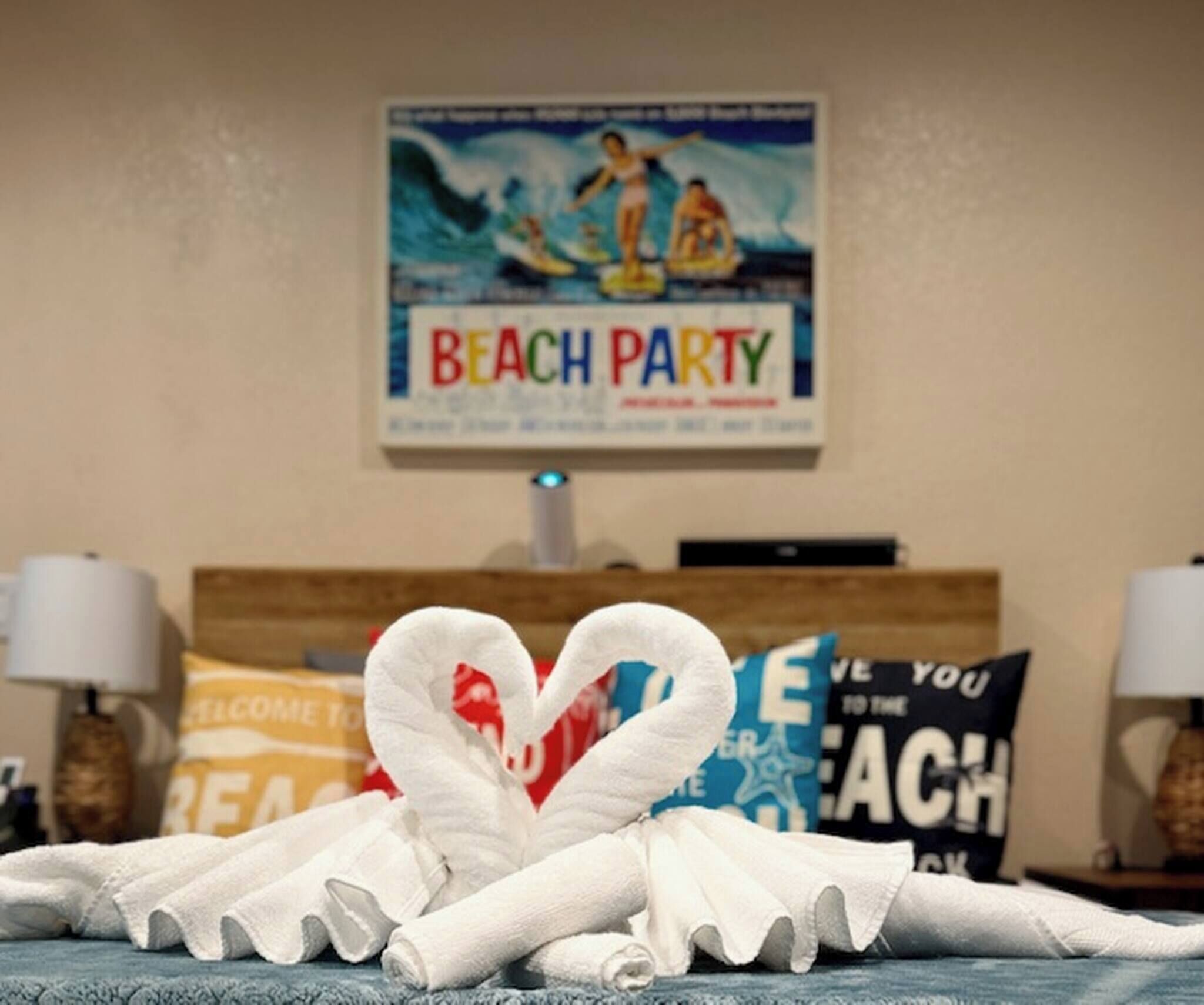 Una habitación de hotel con una cama, un cartel en la pared que dice "BEACH PARTY" y toallas decorativas.