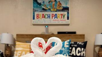 Una habitación de hotel con una cama, un cartel en la pared que dice "BEACH PARTY" y toallas decorativas.