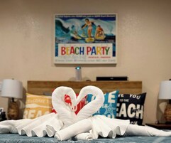 Una habitación de hotel con una cama, un cartel en la pared que dice "BEACH PARTY" y toallas decorativas.