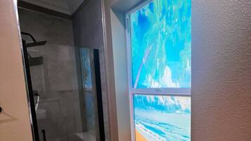 Casa de banho com cabine de chuveiro em vidro, janela com vista para a praia e chão em mármore.