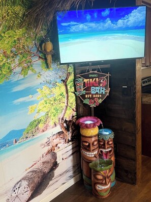 A tiki bar with a beach mural, a television screen, and wooden totem poles. - Tropical Spa Studio, Jacuzzi, Kitchen, Sparks (Sparks)