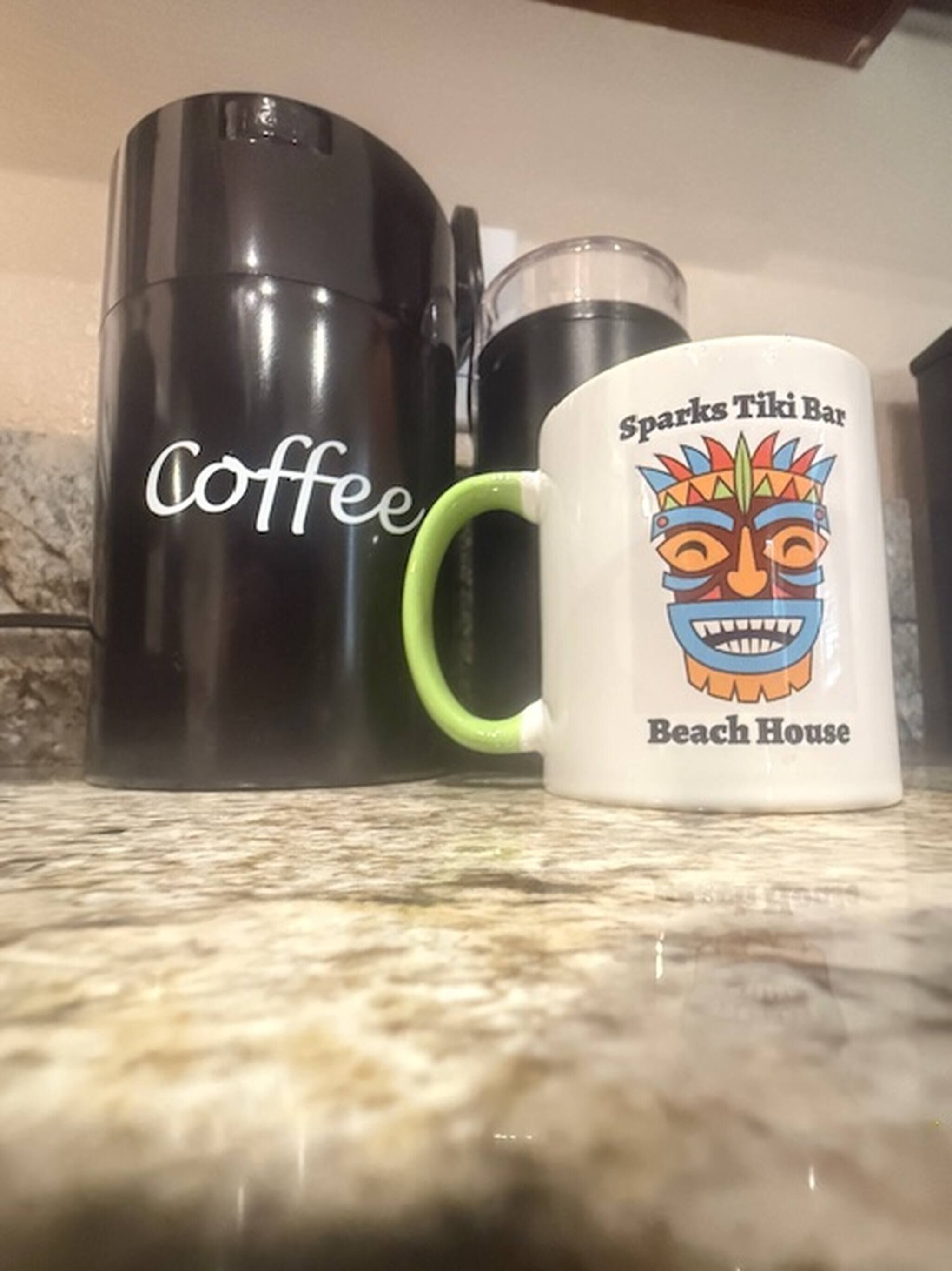 Une machine à café et une tasse décorée d’un motif de bar tiki, posés sur un plan de travail de cuisine.