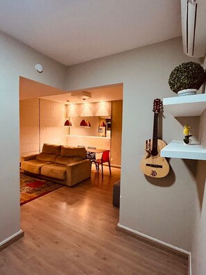 A living room with a sofa, a small table, a guitar, and a wall-mounted shelf with decorative items. - Cozy apartment in Copacabana for 4 people. Near the beach, Post 05. (Rio de Janeiro)