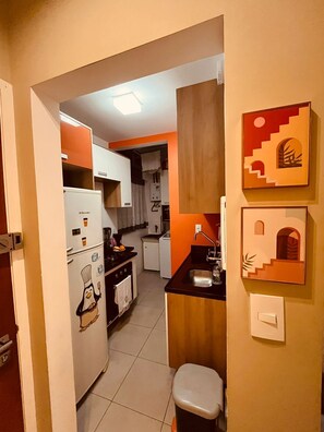 Eine kleine Küche mit Kühlschrank, Backofen und Spüle, sowie ein kleiner Hocker.