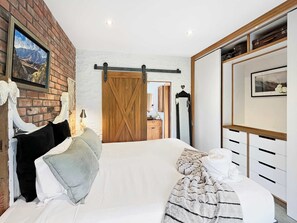 A bedroom with a large bed, a wooden door, a dresser, and a mirror. - The Shed: Rustic Retreat with Modern Comfort (Queenstown)