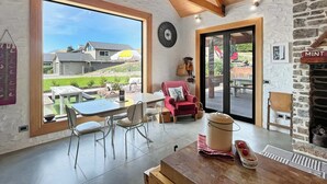 Una habitación amplia con un ventanal grande, una mesa de comedor, sillas, un sillón rojo y una chimenea de piedra.