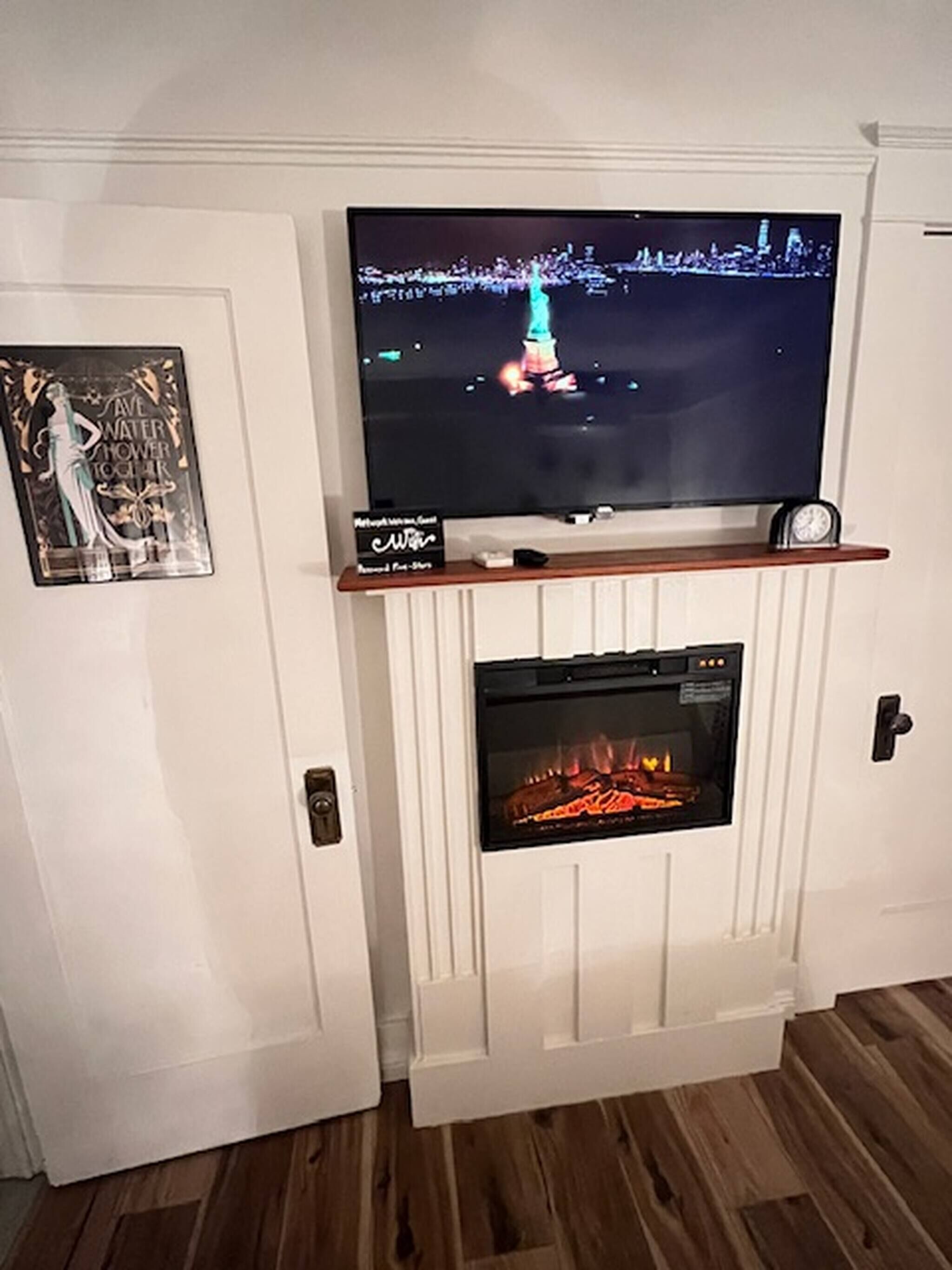Una chimenea con un televisor montado arriba, un reloj y un cuadro en la pared.