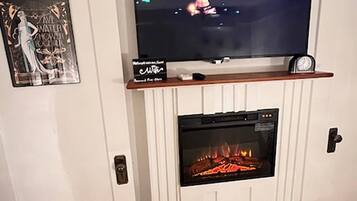 Una chimenea con un televisor montado arriba, un reloj y un cuadro en la pared.