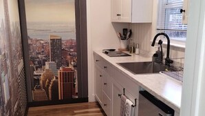 A compact kitchen with a cityscape view through a glass door, wooden flooring, and a small sink. - Deco Studio Retreat With Fireplace, Wifi, Queen Bed (Reno)