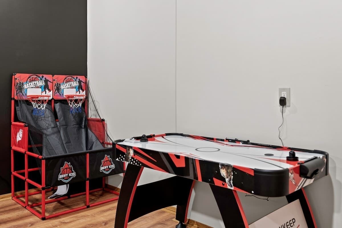 Een tafelvoetbalspel klaar voor gebruik, met een tafel in rood en zwart, twee stoelen met een basketbalthema, en een stopcontact aan de muur.