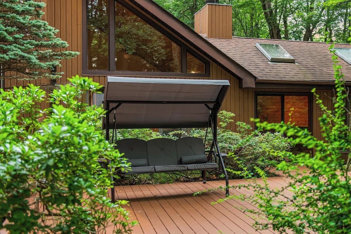 Een modern huis met een houten terras, een overdekte zithoek en grote ramen.