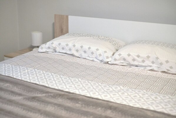 Cama bem arrumada com roupa de cama estampada e travesseiros, um abajur e uma cabeceira de madeira.