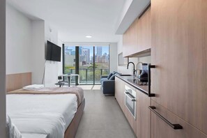 Ein modernes Hotelzimmer mit Bett, Küchenzeile und einem Balkon mit Blick auf die Stadt.