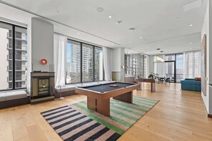 Ein modernes Wohnzimmer mit Billardtisch, großen Fenstern und Blick auf die Stadt.