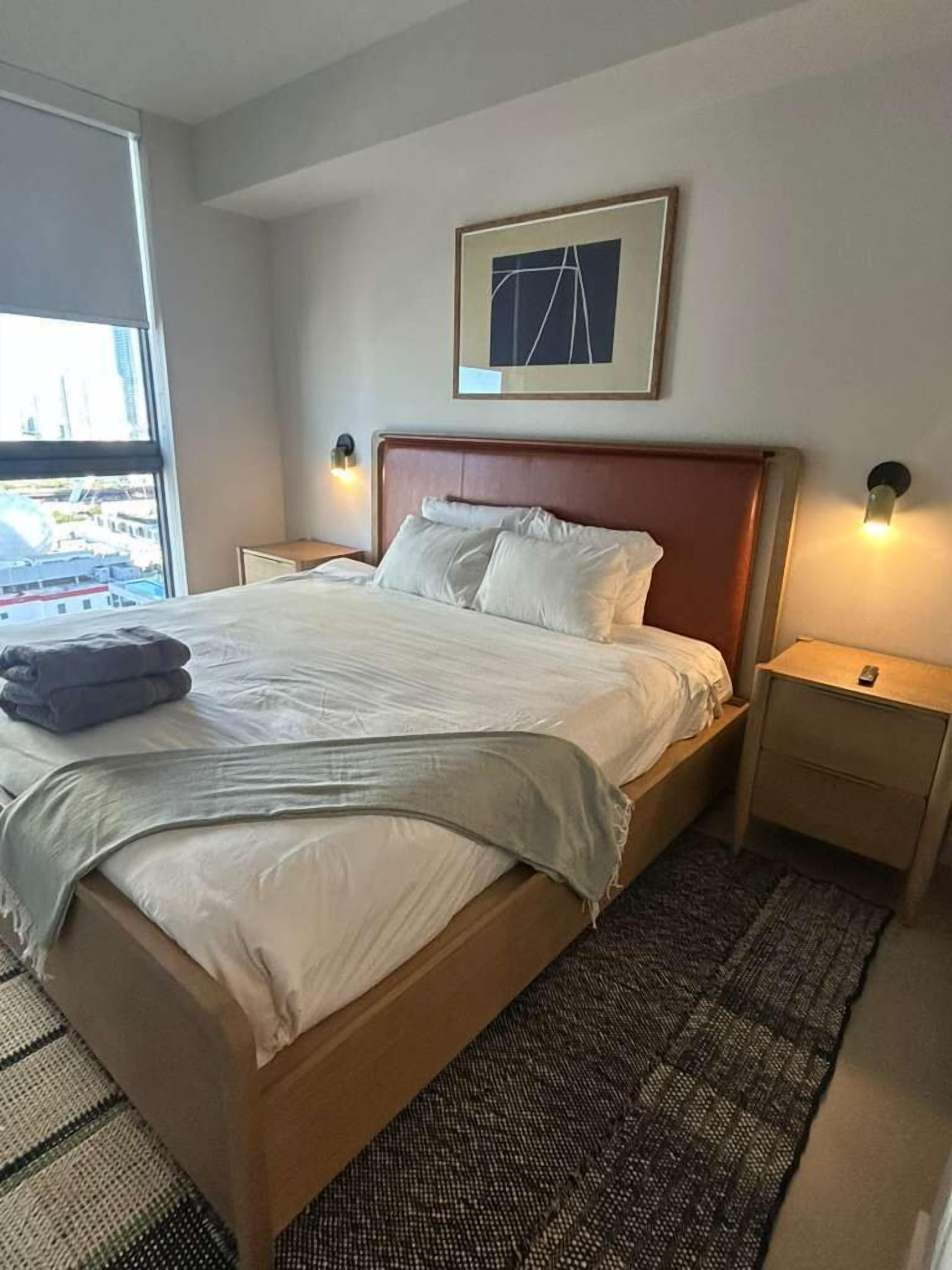 Ein Hotelzimmer mit einem großen Bett, Blick auf die Stadt durch ein Fenster und einem gerahmten Bild an der Wand.