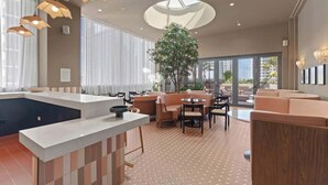 Een moderne hotellobby met een centraal eiland, zithoeken en een groot raam met uitzicht op de omgeving.
