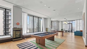 Een moderne woonkamer met een pooltafel, grote ramen en uitzicht op de stad.