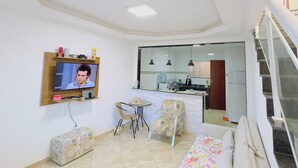 A living room with a sofa, a television, and a small dining table with chairs. - Deruci Beach House (Cabo Frio)