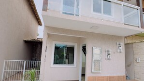 A two-story house with a balcony, a tiled patio, and a potted plant. - Deruci Beach House (Cabo Frio)