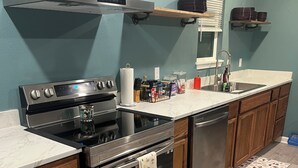 Moderni keittiö, jossa on ruostumattomasta teräksestä valmistetut kodinkoneet, puukaapit ja marmoritaso.