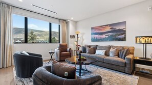 A living room with a sofa, armchair, and a coffee table. There is a large window with a view of a landscape. - Mountain Dream at Frontgate by Avantstay Condo + Ski Shuttle Pool + Spa Access Mins to Beaver Creek (Avon)