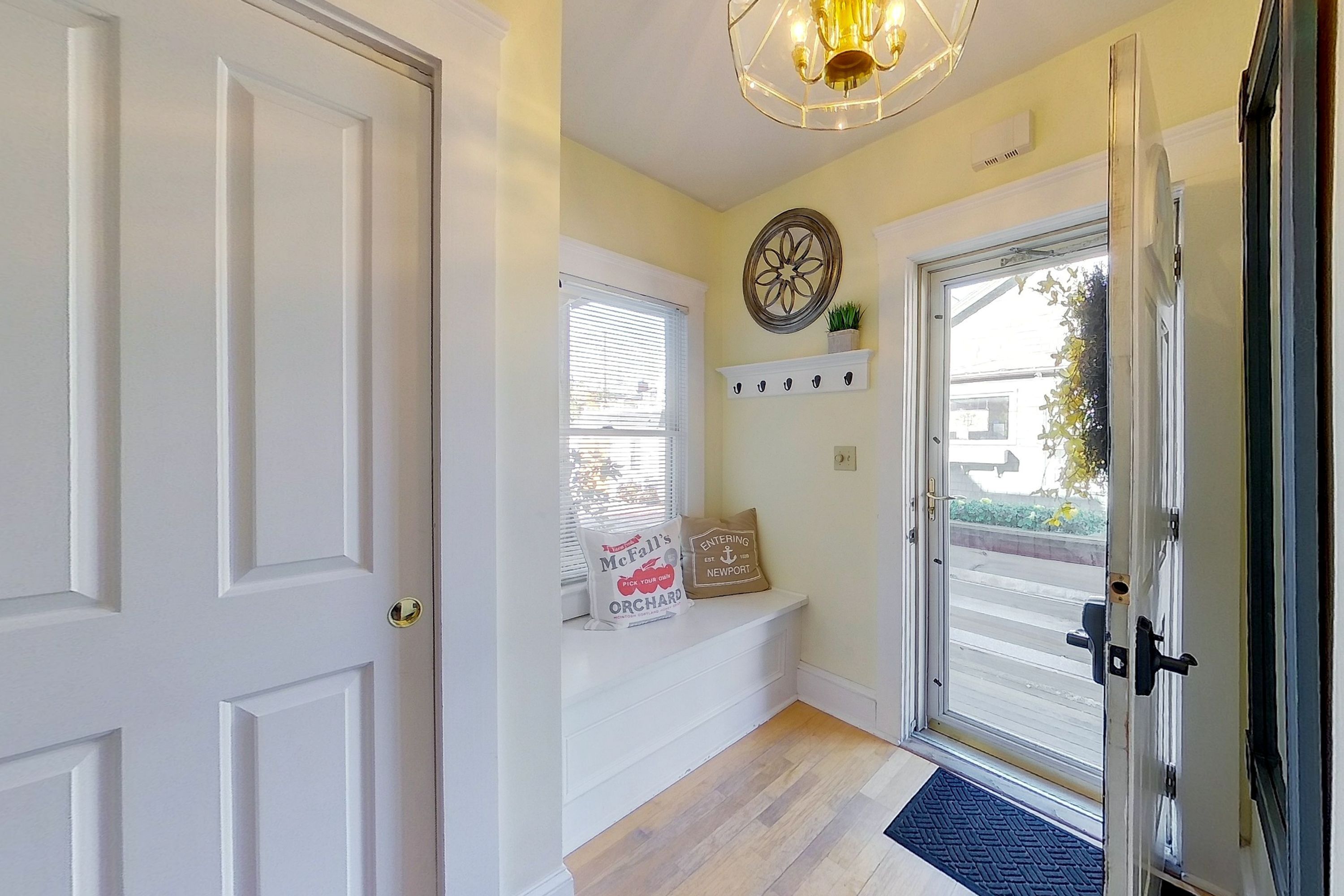 A hallway with a bench, a decorative wall piece, and a door leading outside.