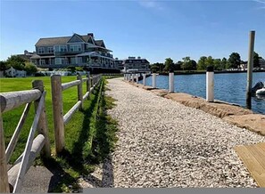 Un paseo marítimo con valla de madera, guijarros y un muelle que se adentra en el agua.