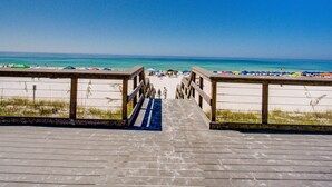 En träpromenad som leder till en strand med parasoller och folk.