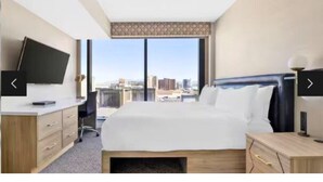 A hotel room with a large bed, a desk, a chair, a TV, and a city view. - Hilton Grand Vacations Club Elara Center Strip Las Vegas
1-bedroom suite (Las Vegas)