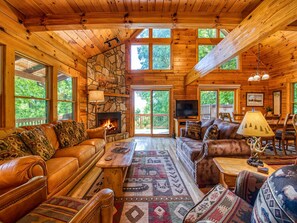A log cabin interior with a stone fireplace, leather sofas, a TV, and a dining area. - Hickory Ridge Getaway | Log Cabin with Hot Tub, Fire Pit, & Game Room Near Maggie Valley (Maggie Valley)